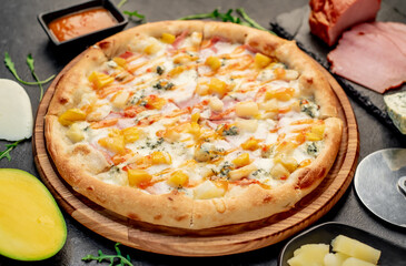 delicious pizza with ham, cheese, pineapple, mango on a stone background