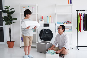 Smiling Asian father and little boy child is hugging for enjoying and Washing together in Laundry room on holiday. Family activities and child educational for homeschool concept.