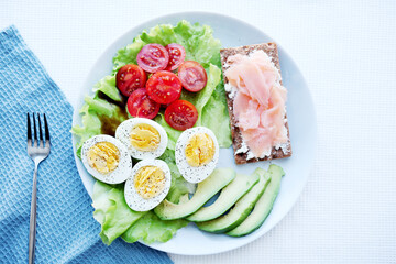 Ketogenic paleo diet. Boiled eggs, salmon toast, tomatoes, avocado and fresh salad. Healthy breakfast.