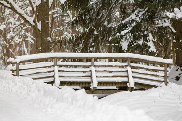 Forest covered with recently fallen, white fluffy snow. In the foreground, the wooden railing of the small bridge is also covered with snow. Selective focus.