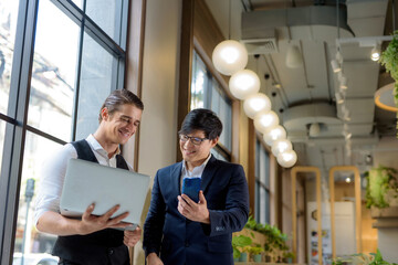 2 business people positive A white man pointed to The computer of an Asian man working together in the workspace.