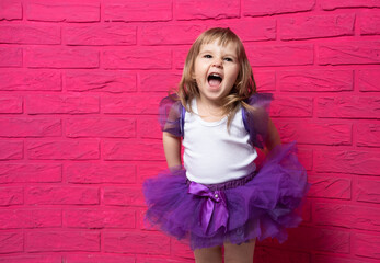 carefree cute little girl in tutu skirt laughing out loud giggling on pink background