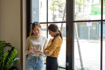 The two Asia use phone see content Social media Front window in coffee shop.