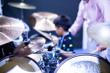 Blurry kid learning and play drum set with music teacher in music room. The concept of musical instrument. Blurry music background.