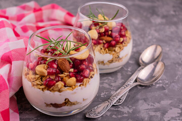 Dessert with cream cheese with muesli and pomegranate in glasses on a gray background.
