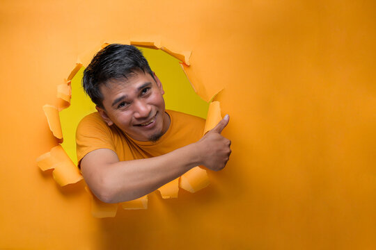 Asian man with happy expression pointing a copy space to advertise something, on torn paper hole