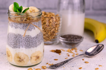 Chia pudding with banana and granola in a jar on a white background.
Close-up.