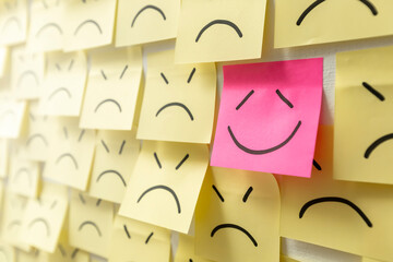 A sign of a drawn smile on a sticker against a background of sad faces of icons. Business success symbol.