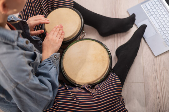 A faceless woman sits on the floor at home and watches educational videos of playing mini bongs. Girl remotely learns to play traditional ethnic drums.