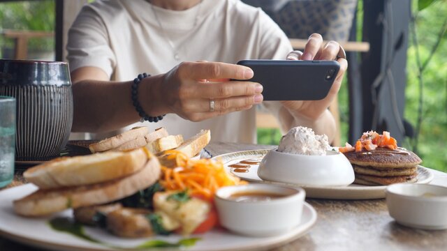 Close of human hands taking pictures of food served on a wooden table. Vegan breakfast as content for food blog