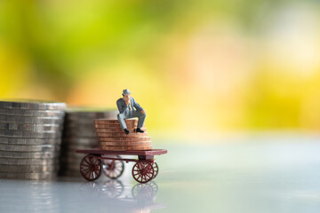 Miniature : Businessman sitting on a coin truck behind a coin, green nature background.