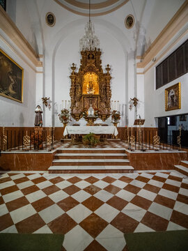 Interior view of a side chapel in the Church of Santa Maria la Mayor in Ronda, Spain, showing a gilded Baroque altarpiece, marble steps, and a brown and white checkered tile floor.