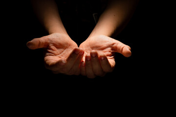 Two hands with open palms turned up, offering or giving something, a handful. Hands on a black background, contrasting dramatic light from above