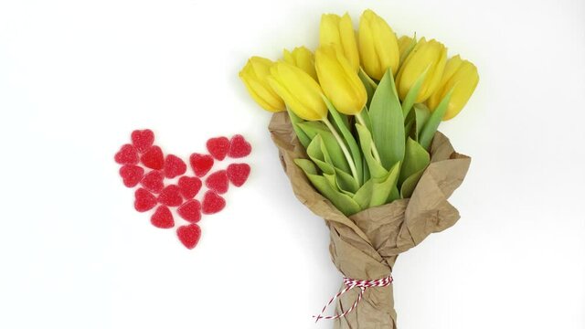 a bouquet of yellow tulips and a red candy heart on white, flat lay top view