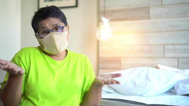 Senior Asian woman with Covid-19 health care prevent for New normal lifestyle safety quarantine, wearing protective face mask protecting herself from sickness coronavirus influenza in bedroom