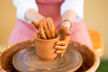Woman hands sculpts cup from clay pot. Workshop of modeling on potter wheel.