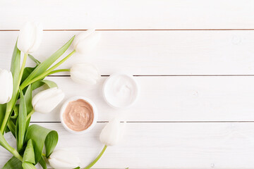 Obraz na płótnie Canvas Cosmetic creams with white tulips top view flat lay on white wooden background