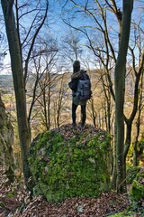 Fototapeta premium Eine junge Frau steht auf einem großen, moosbedeckten Stein und blickt auf das Altmühltal in Bayern, Deutschland.