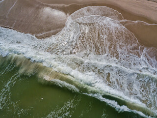 Fototapeta na wymiar Aerial drone image of foamy waves washing up on the beautiful sandy beach of Island Beach State Park in New Jersey creating colorful abstract images