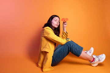 Launch a paper airplane, a dream travel concept. Young brunette woman in yellow sitting on a yellow background, studio shot.