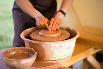 Hands of potte makes pottery dishes on potter's wheel. Sculptor in workshop makes clay product closeup