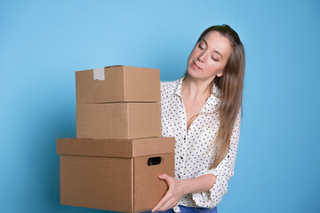 Accept a parcel, happy young woman holding a stack of cardboard boxes, portrait on a blue background