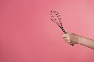 Whisk for whipping cream, making desserts. A woman's hand and kitchen tools. pastry chef on a pink background. copy space