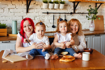 Two mothers with young children and daughters together in the kitchen.