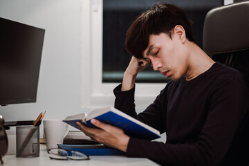 Young handsome asian man sleeping from heavy reading book at work desk late at night, Knowledge and learning concept.