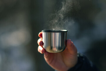 Thermos with hot tea in hand, steam from hot drink