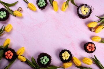 yellow tulips and bird nests with colored eggs on a pink background, Easter holiday greeting card. Top view. Copy space