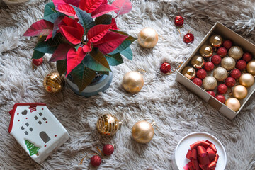 Christmas and New Year decorations. Box with red and gold Christmas balls on a soft light blanket against the background of the traditional Christmas flower Poinsettia. New Year's decor in red colors