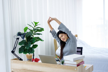 An Asian woman worked and stretched on the desk in his bedroom..