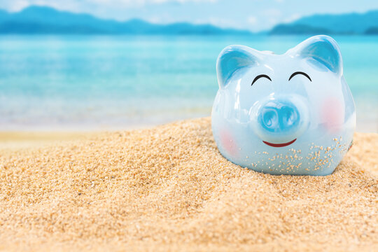 Summer happy piggy bank on sand beach over blurred tropical blue sea background, image for saving vacation concept.