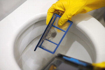 Hands in rubber gloves throw out trash in toilet, close up.