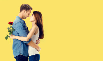 Naklejka premium Love, relationship, dating, flirting, romantic concept - amorous hugging couple with flower, standing close to each other. Studio portrait of young man and woman, isolated over yellow background.