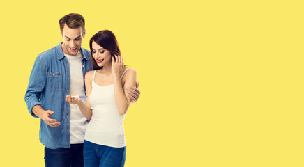 Love, new parents and happy family concept - happy couple, finding out results of a pregnancy test. Studio portrait of young man and woman, isolated over yellow background.