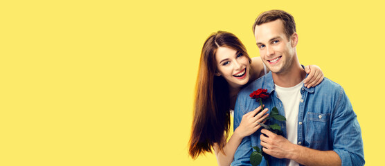 Love, relationship, dating, flirting, romantic concept - happy couple with flower, looking at camera. Studio portrait of young man and woman, isolated over yellow background.