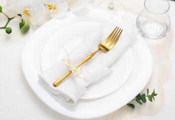 Spring, festive table setting with white napkin and white flowers on a light tablecloth