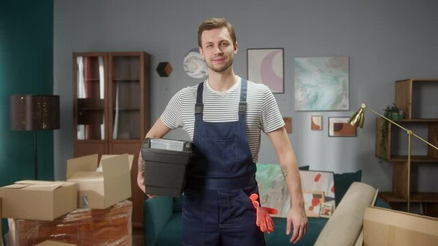 Portrait of smiling repairman worker with tool box, man preparing to move boxes and build furniture in room, craftsman looking at camera. Moving to new flat or apartment. Daylight 
