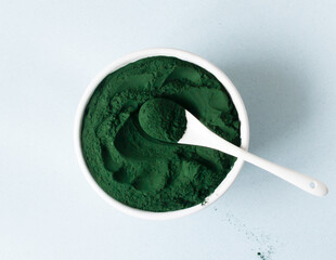 Chlorella powder in a white bowl with a teaspoon on a blue background. Superfood concept....