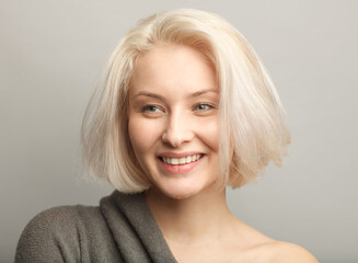 young blonde woman smiling sincerly isolated on gray background, close up portrait