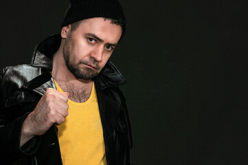 Portrait of a man in a black hat on a dark background. Young stylish hipster with beard dressed in black jacket