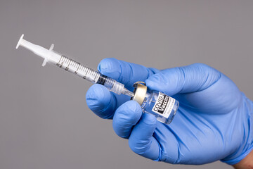 Close-up of hand with surgical glove insert syringe into covid-19 vaccine vial
