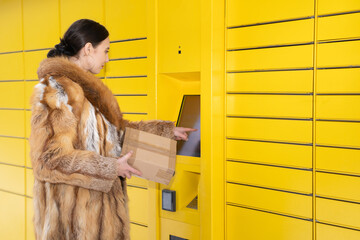 A rich woman in a fur coat operates the touchscreen of a parcel locker. Receive and send parcels...