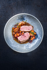 Modern style traditional roasted dry aged veal tenderloin with jus and braised winter root vegetable served as close-up in a design bowl