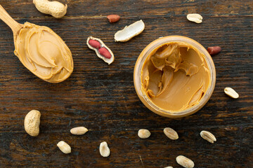 Wooden spoon with a jar of peanut butter and a bunch of scattered nuts