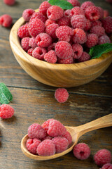 Fresh raspberries in a wooden plate with leaves. The berries are scattered on a wooden table.