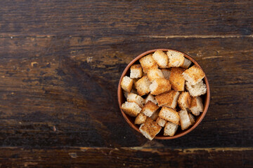 Crispy croutons in a bowl on a wooden background.