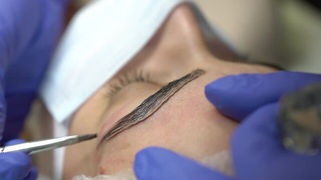 Professional beautician treatment concept. Close up portrait, young woman getting eyebrow threading, painting, macroblade shaping procedure. Therapist is taking care of eyebrows.